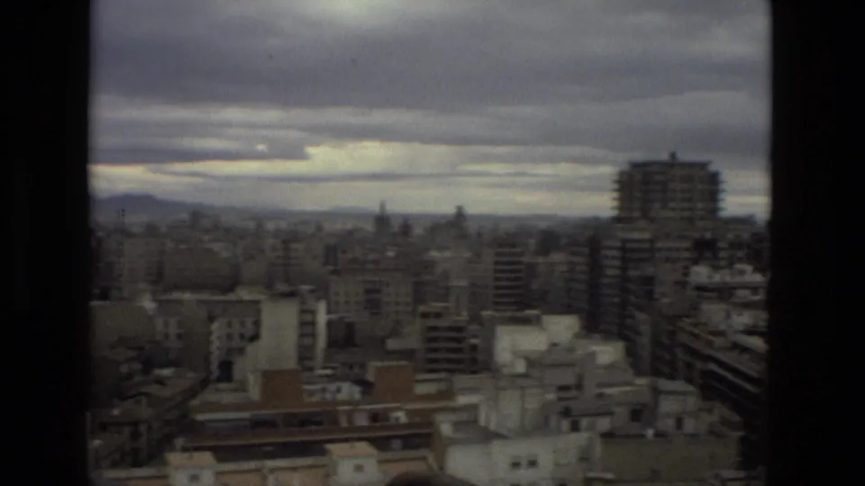 The camera looks across Barcelona's rooftops and taller residential blocks beneath heavy clouds in 1978 8mm footage.