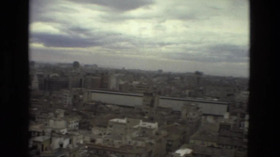 High 1978 Barcelona view with dense buildings, a long pale wall or facade, and a heavy cloudy sky beyond a dark window edge.