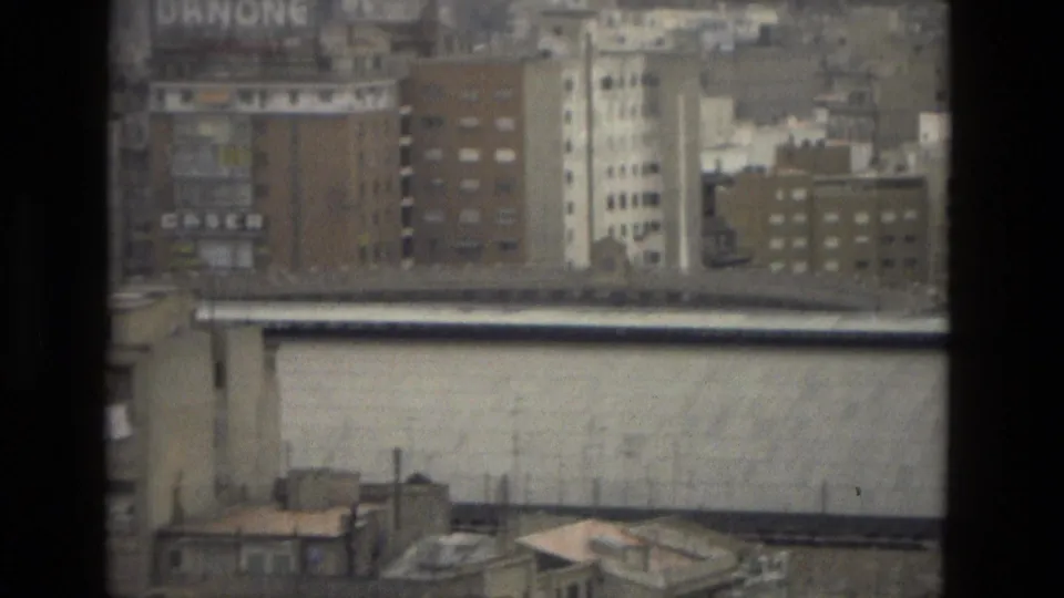 Closer 1978 Barcelona urban view through a window, showing apartment blocks, rooftops, a pale wall, and faint visible signage.
