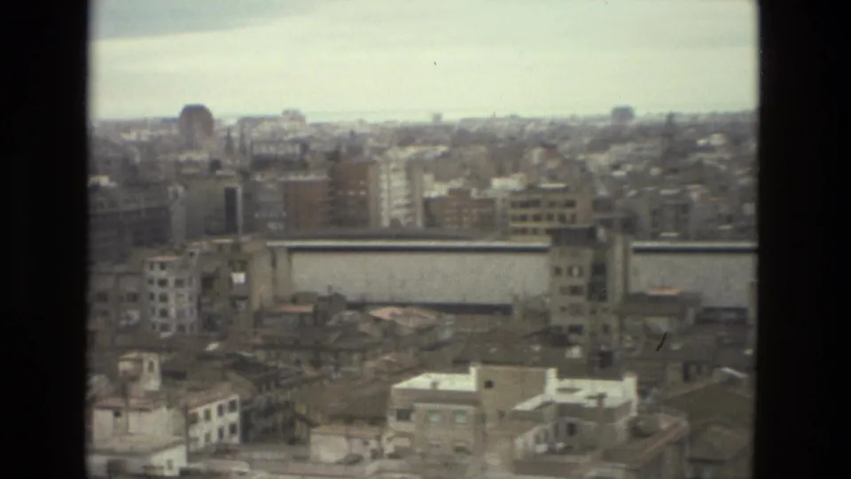 1978 Barcelona cityscape from a high vantage point, with rooftops, mid-rise buildings, and an overcast sky framed by dark window-like borders.