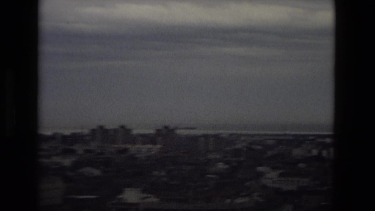 Hazy city skyline and distant coast seen through dark film-frame borders.