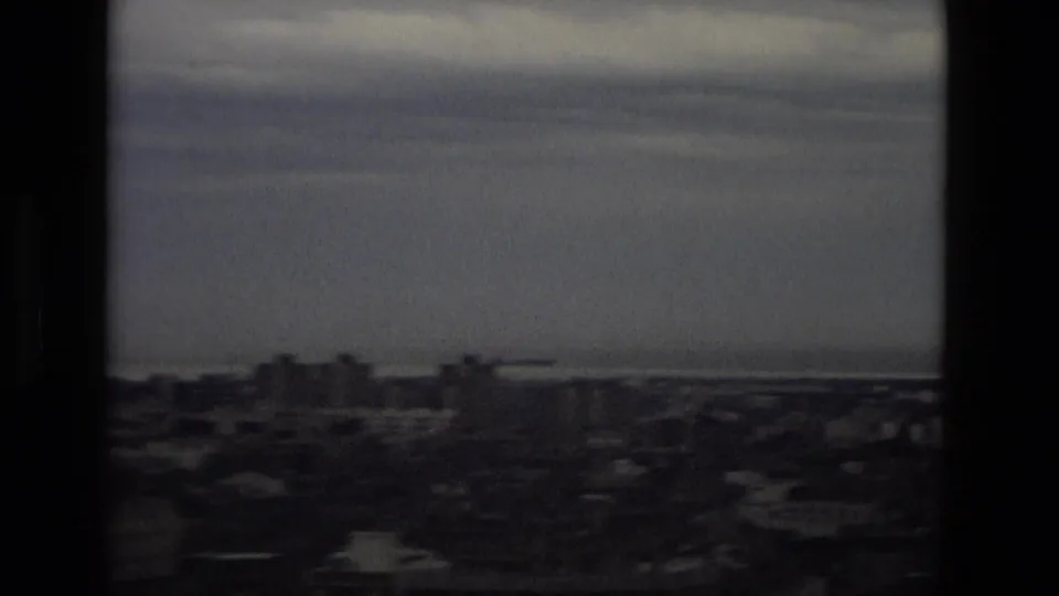 1978 Barcelona city view with low rooftops, distant coastline, soft haze, and dark window-like borders.