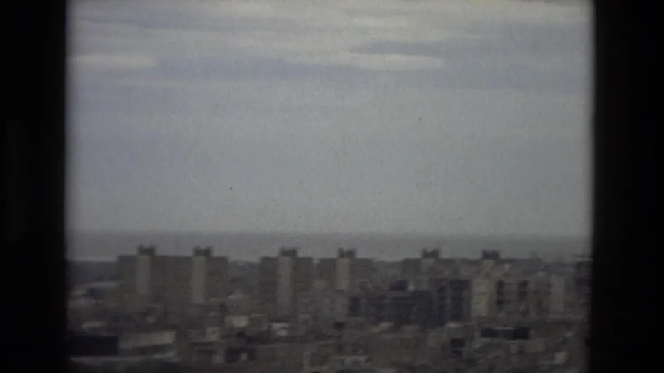 Elevated 1978 Barcelona view showing apartment towers, dense rooftops, and a faint sea horizon.