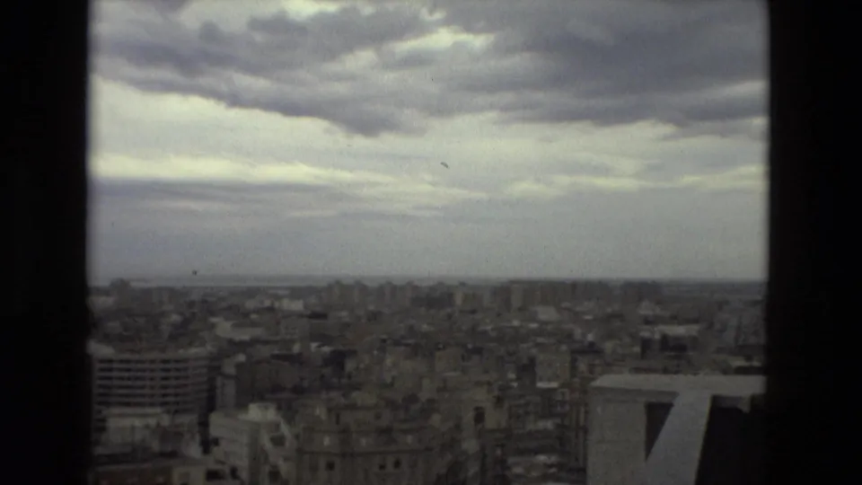 Wide 1978 Barcelona cityscape with dense rooftops, mid-rise structures, and dramatic overcast clouds.