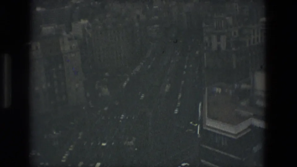Dark, glass-reflected 8mm frame showing Barcelona streets, traffic traces, and buildings from an elevated interior viewpoint.