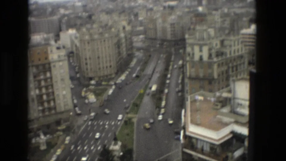 1978 Barcelona street grid from above, with apartment buildings, multi-lane roads, cars, buses, and a corner rooftop in view.