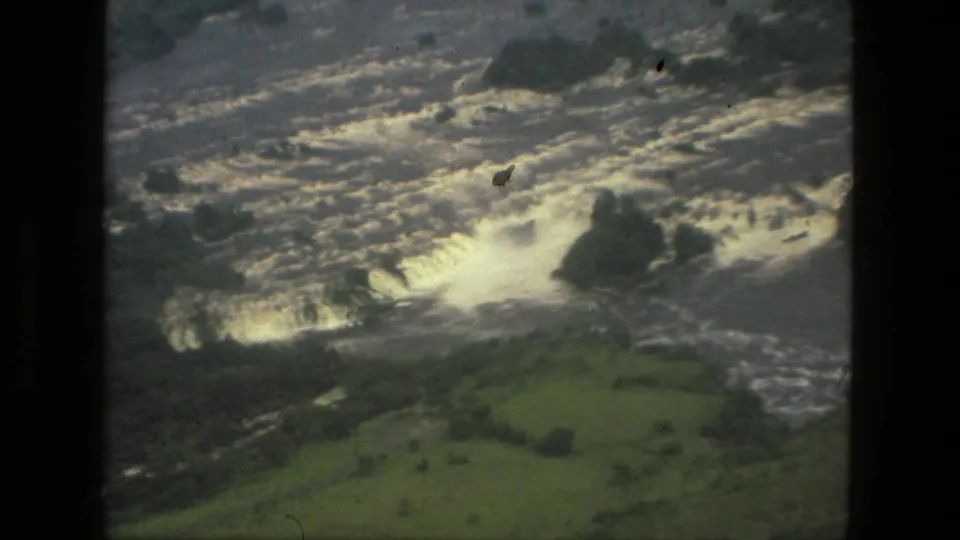 1979 Manaus-area aerial frame showing white water over a waterfall or rapids, with green forested terrain around the river.