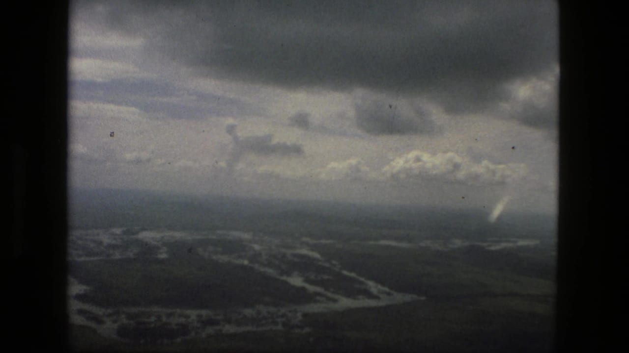 1979 Manaus aerial frame with heavy clouds, hazy horizon, and flooded river channels across dark green terrain.