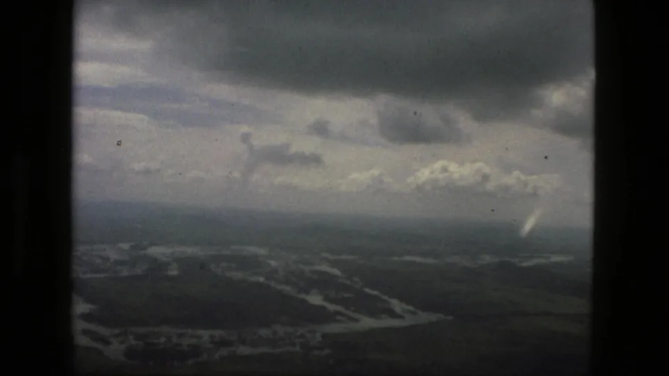1979 Manaus aerial frame with heavy clouds, hazy horizon, and flooded river channels across dark green terrain.