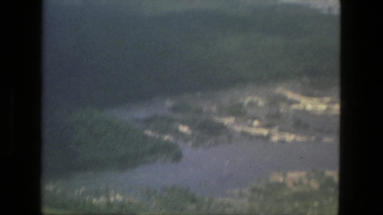 1979 Manaus, Brazil aerial 8mm frame showing water channels, tropical greenery, clouds, and soft focus from an aircraft viewpoint.