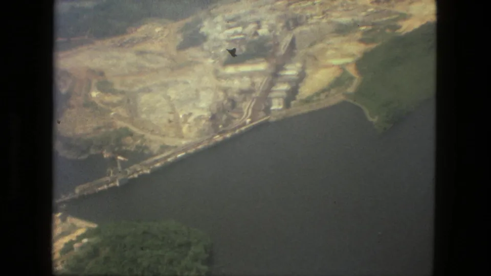 1979 Manaus, Brazil aerial frame showing a riverfront construction or industrial area beside water, bordered by dense greenery.