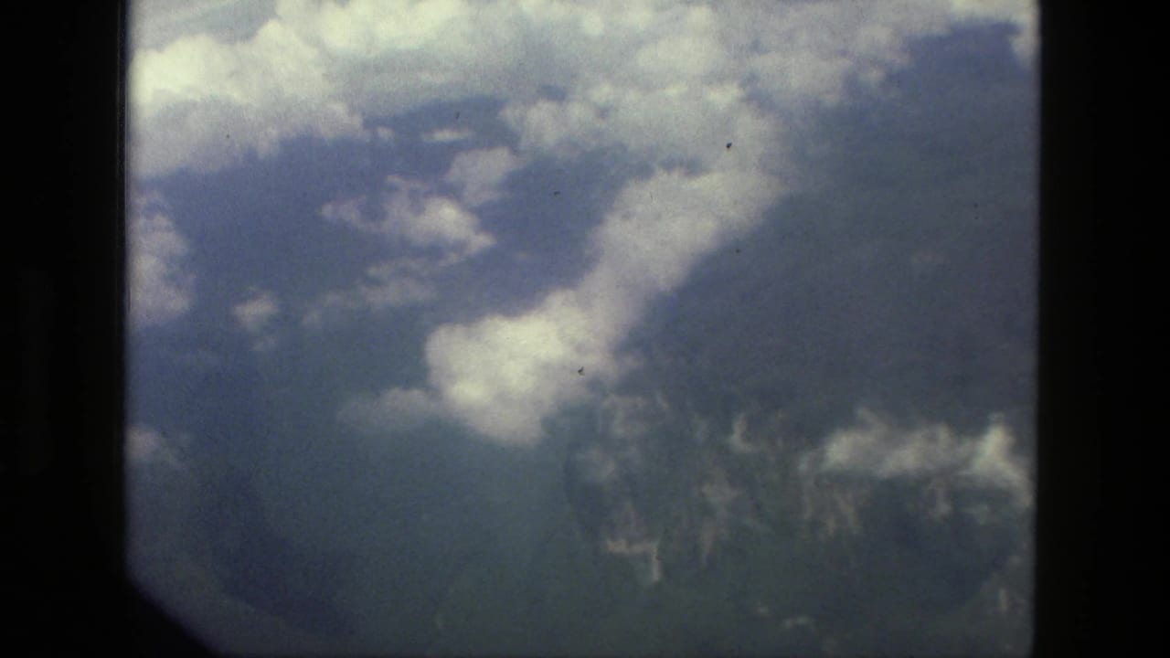 1979 8mm plane-window view near Manaus, Brazil, showing clouds over hazy ridges, water, and forested land.