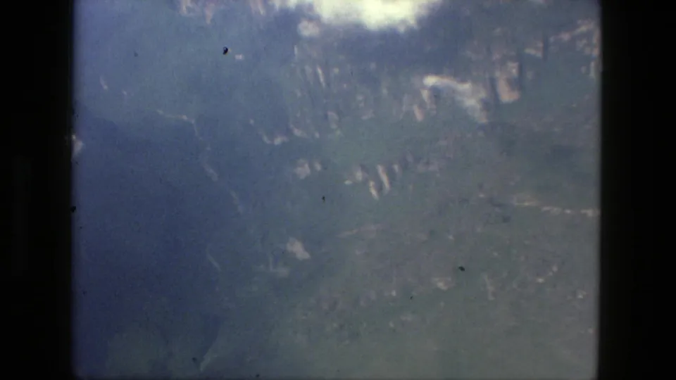 1979 8mm aerial view near Manaus, Brazil, showing cloud cover, blue water, green terrain, and dark plane-window framing.