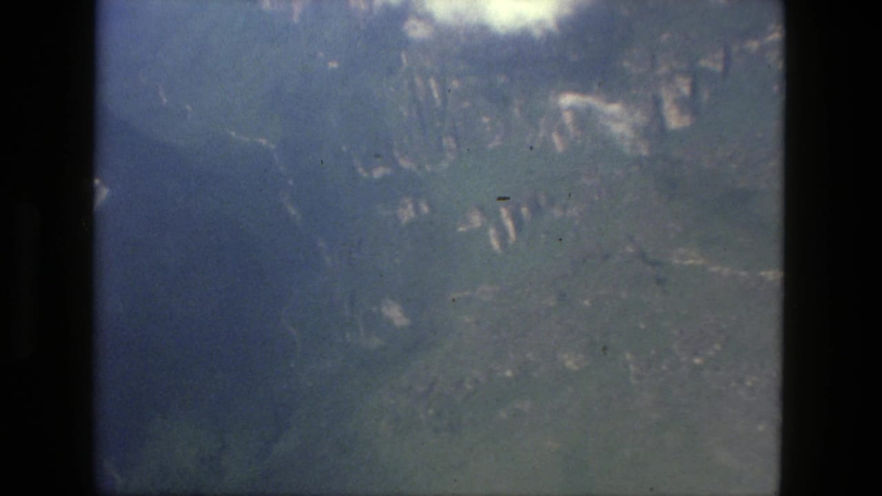 Soft aerial view of green mountains and valley terrain through an 8mm film frame.