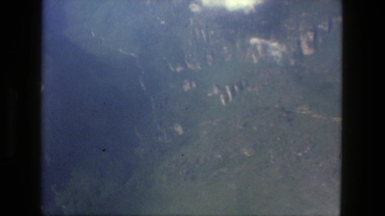 Aerial view of forested hills and valley shapes beneath a hazy sky.