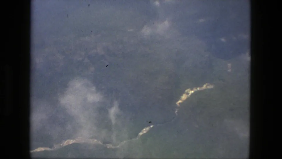1979 Manaus, Brazil aerial 8mm frame showing clouds over green terrain with bright water or shoreline-like edges.