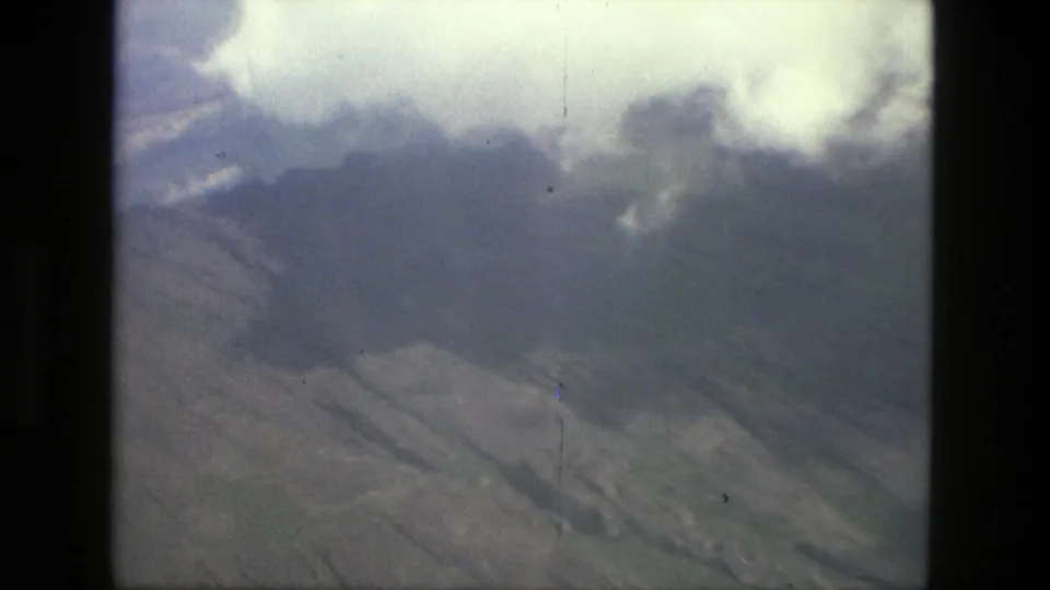 1979 Manaus, Brazil aerial frame showing cloud cover, mountain ridges, and shadowed valley terrain.