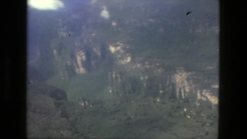 Aerial frame from the 1979 Manaus reel showing forested terrain, pale exposed slopes, cloud patches, and dark film borders.