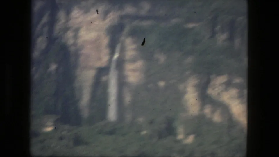 1979 Manaus-area 8mm frame with a narrow waterfall descending a forested cliff, softened by grain and exposure haze.