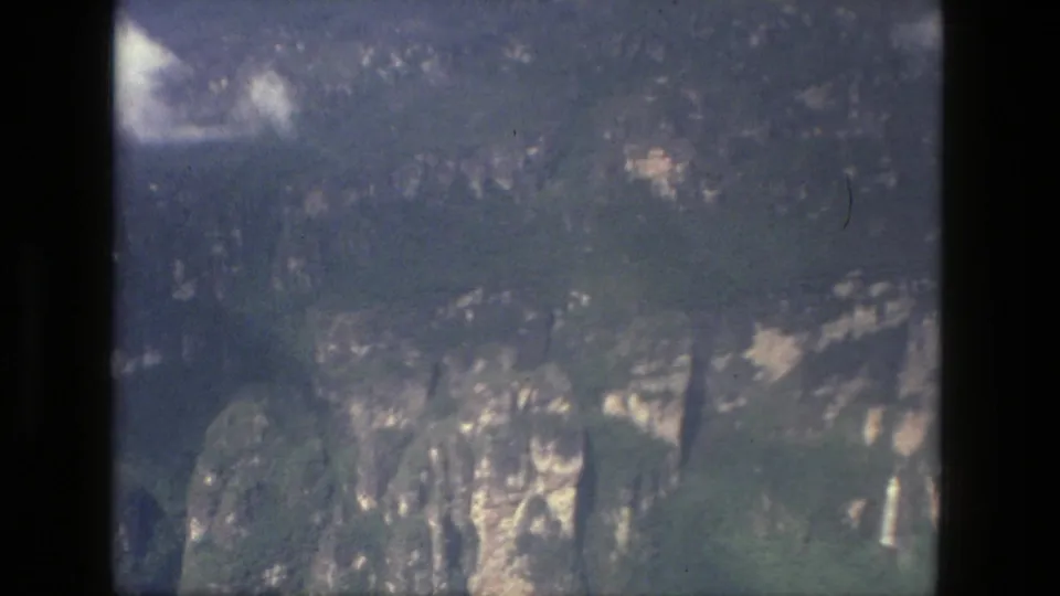 1979 Manaus metadata frame showing a distant green cliff landscape with pale rock patches, heavy shadow, and visible 8mm borders.