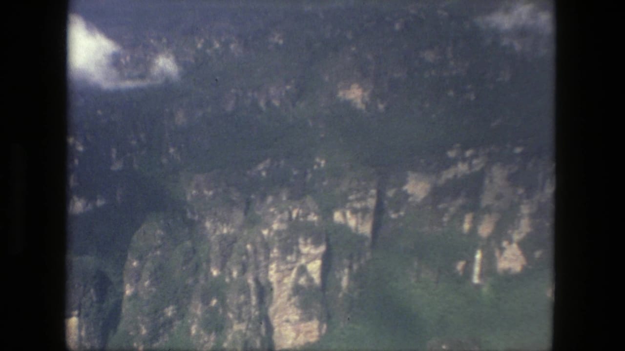 Aerial view of forested cliffs and pale rock faces through a dark film frame edge.