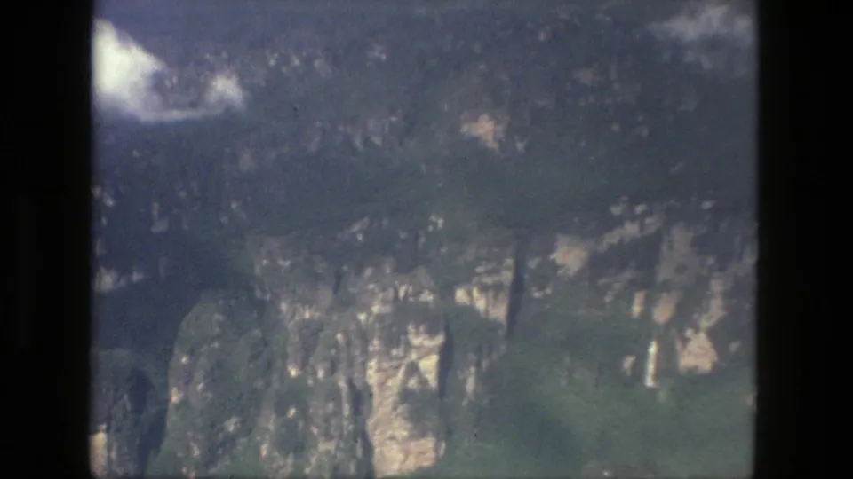 1979 8mm aerial view near Manaus, Brazil, showing dense green vegetation over steep pale stone cliffs with soft focus and film grain.