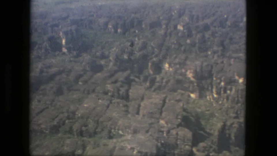 1979 8mm aerial view near Manaus, Brazil, showing rugged stone terrain, tree-covered slopes, haze, and soft vintage color.