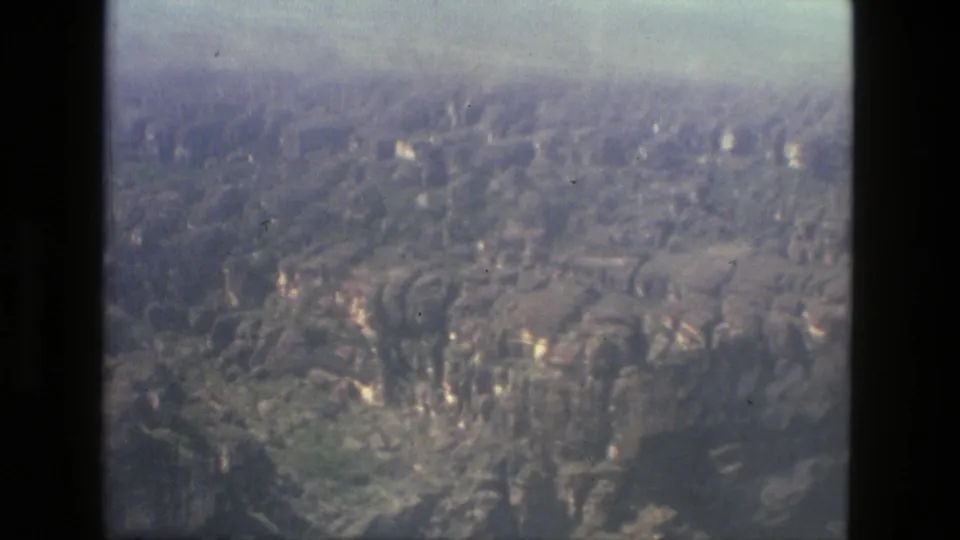 1979 aerial home-movie frame near Manaus with hazy forested slopes, rocky surfaces, and visible 8mm scan texture.