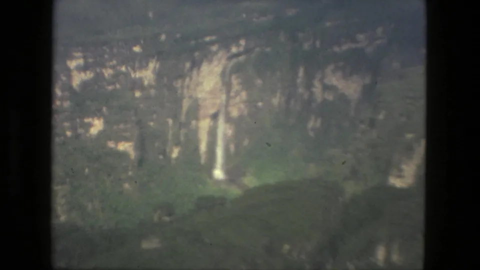 Aerial 8mm frame near Manaus showing a pale waterfall against rocky cliffs and surrounding green vegetation.