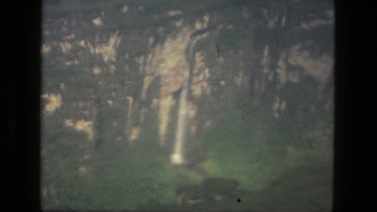 1979 8mm home-movie frame from the Manaus, Brazil metadata showing cliffs, vegetation, and a narrow waterfall.