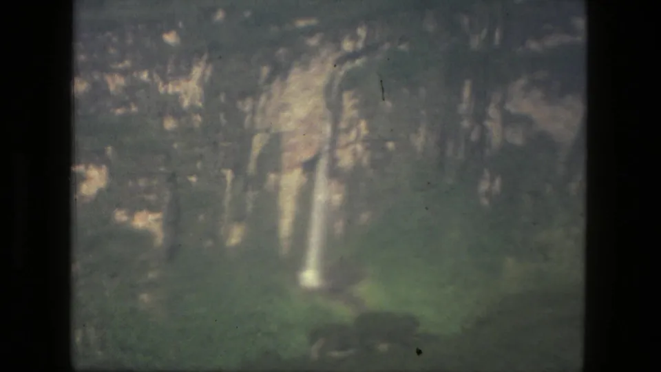 1979 8mm home-movie frame from the Manaus, Brazil metadata showing cliffs, vegetation, and a narrow waterfall.
