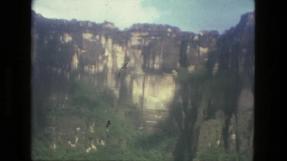 1979 Manaus-area home-movie frame showing pale cliff faces, dark vegetation, and a strip of blue sky.