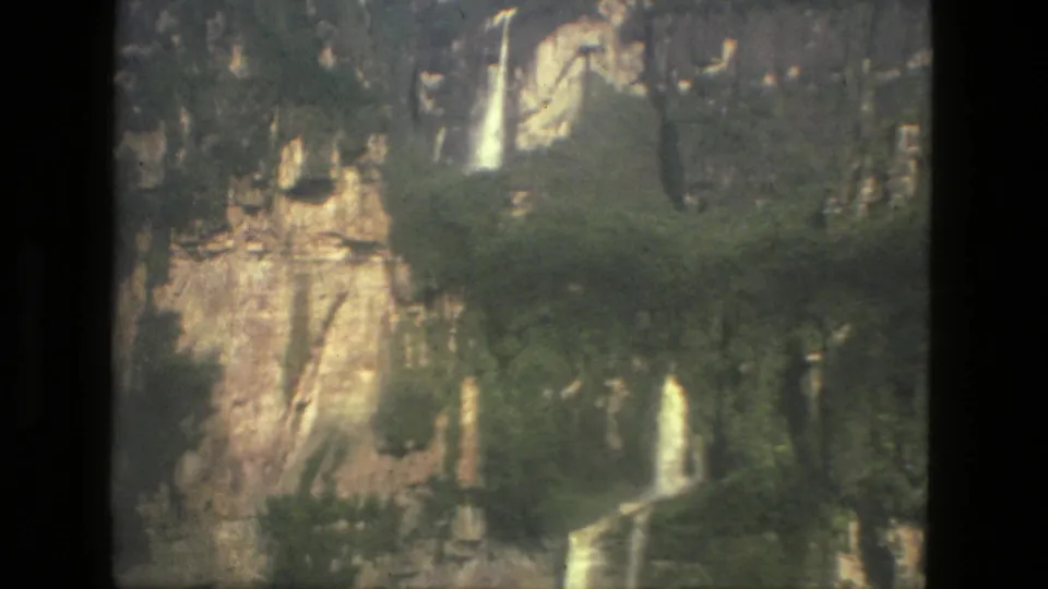 1979 Manaus-area 8mm frame showing a rugged rock face, greenery, and small waterfall drops.