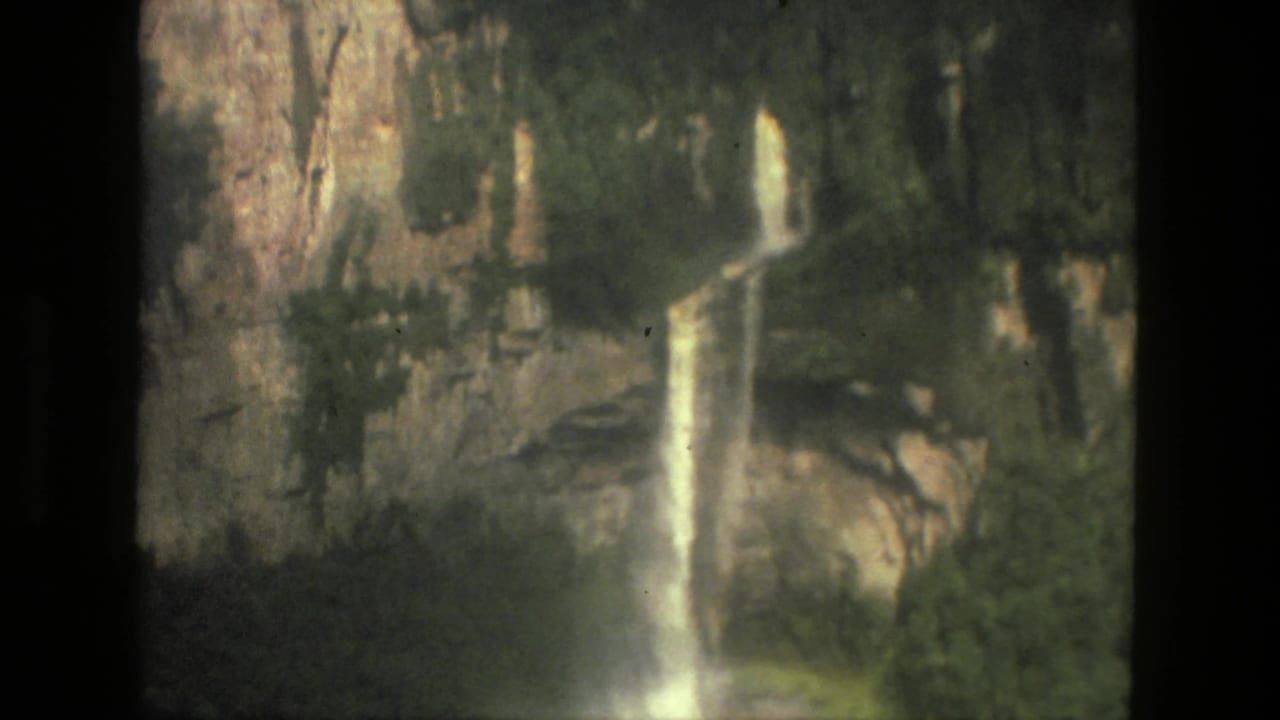 Tall waterfall descending a rocky cliff with green vegetation at the base.