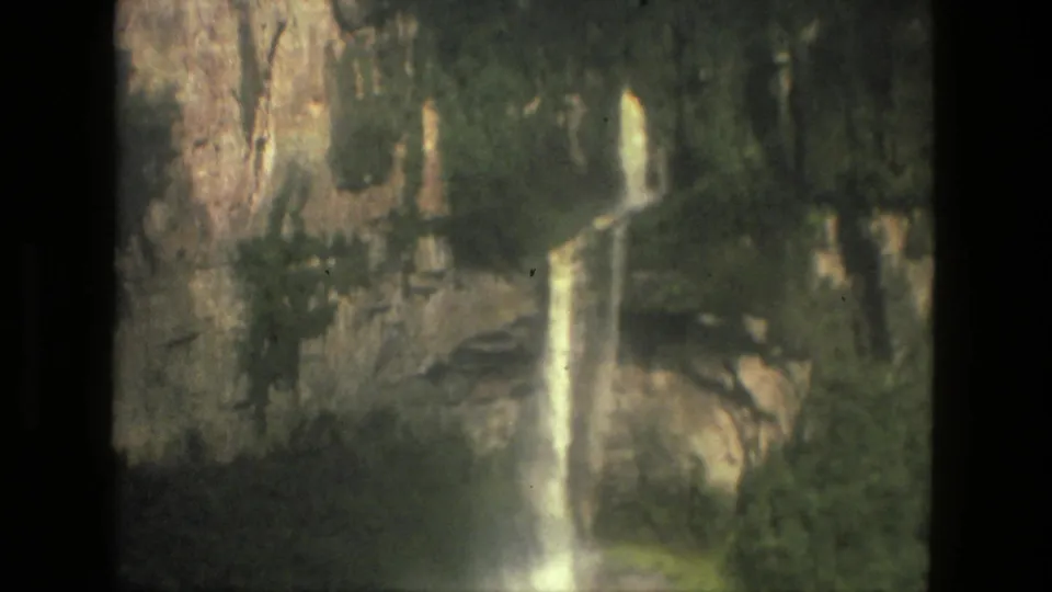1979 8mm Brazil home-movie frame showing a narrow waterfall dropping down a steep cliff with foliage below.