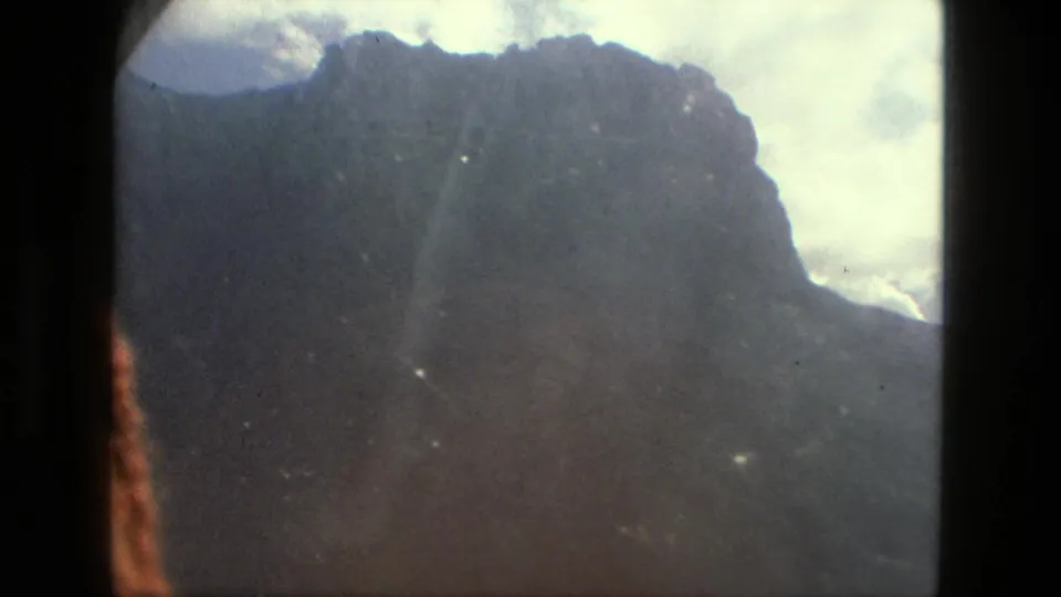 1979 8mm Brazil home-movie frame of a dark mountain ridge under bright clouds, with dust and exposure variation visible.