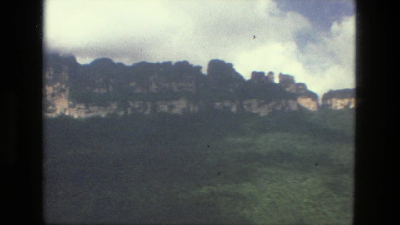 Cloudy mountain ridge with green slopes and pale rock faces seen through an 8mm film frame.
