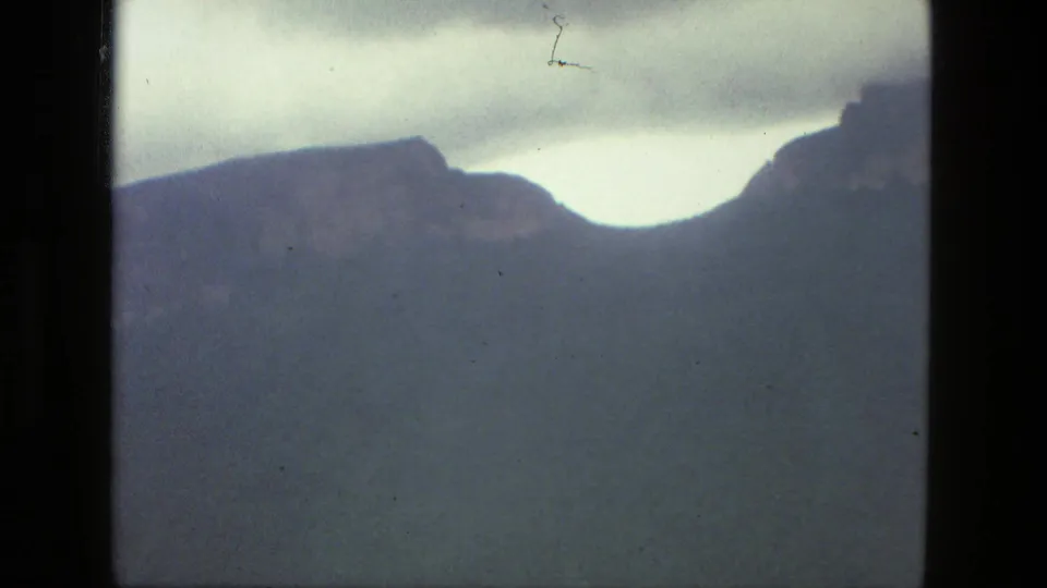 Soft 8mm frame from the 1979 Brazil clip showing a dark ridge against cloudy sky, with visible film dust and a scratch mark.