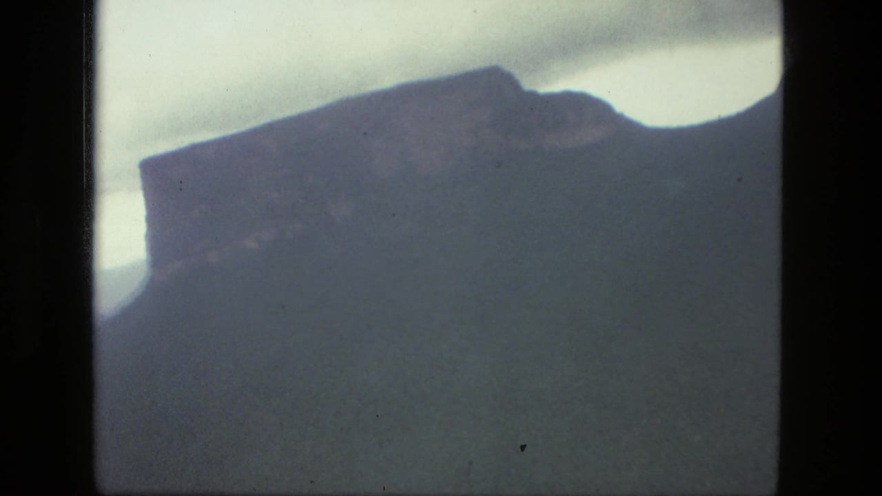 Dark mountain silhouette beneath a pale sky seen through a film frame.