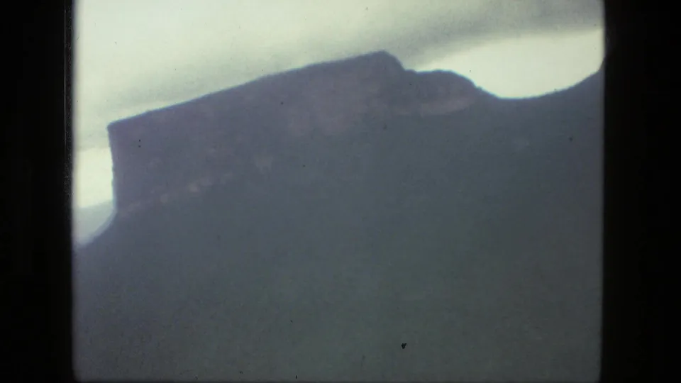 1979 8mm home-movie view near Manaus, Brazil, showing a dark mountain silhouette against a washed pale sky.