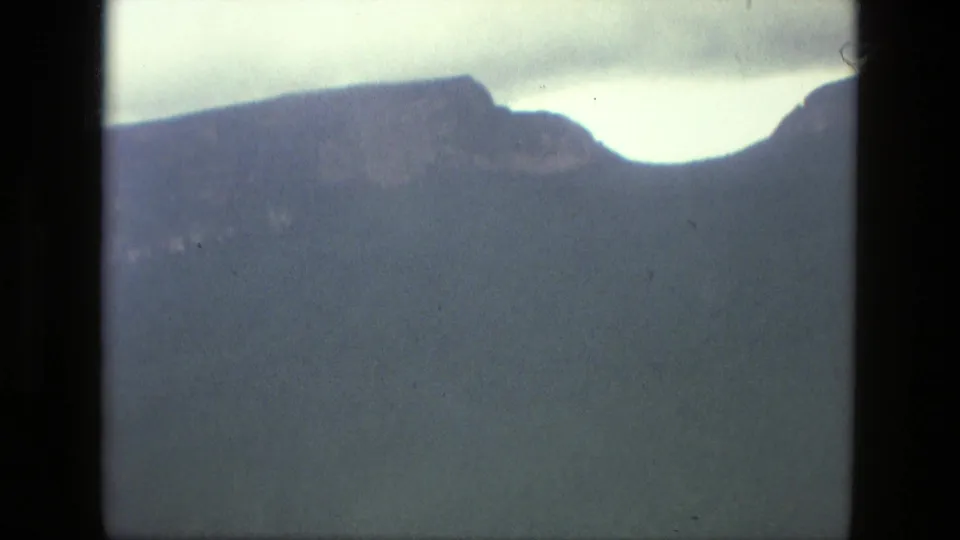 Metadata-supported 1979 aerial view near Manaus showing a dark ridge profile and pale sky through aged 8mm film.