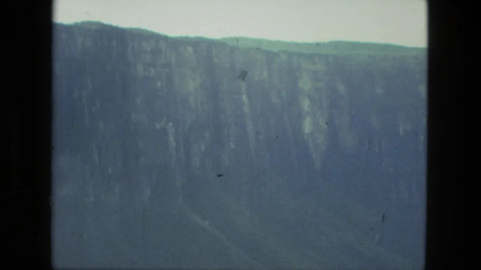 Soft, color-faded 8mm view of a large cliff face and forested ridge during an aerial flight near Manaus.