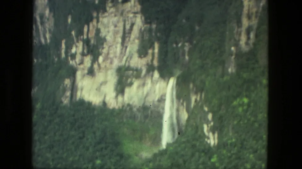 Aerial 8mm view near Manaus of a waterfall descending a rocky cliff amid dense green forest.