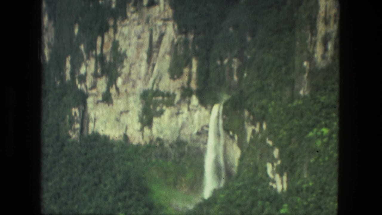 1979 8mm Manaus, Brazil footage showing a waterfall descending from a rugged cliff surrounded by lush vegetation.