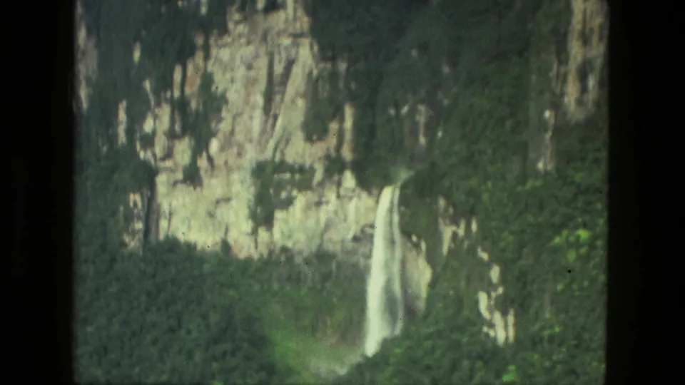 1979 8mm Manaus, Brazil footage showing a waterfall descending from a rugged cliff surrounded by lush vegetation.