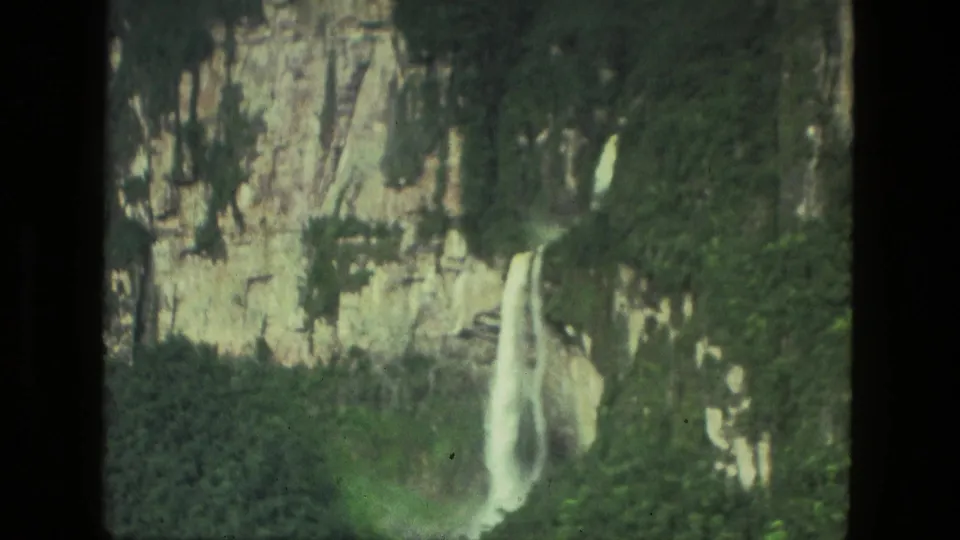 1979 8mm Manaus, Brazil view of a waterfall beside a cliff face, with dense greenery and visible film-frame borders.