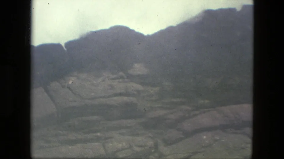 1979 8mm Manaus, Brazil landscape frame showing hazy mountain shapes, a green valley floor, and layered rocks in the foreground.