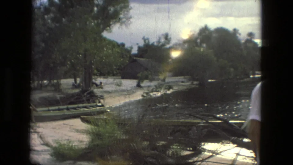 A 1979 Manaus riverside view shows wooden boats along the water, trees, a sandy bank, and a partial figure at the right edge.