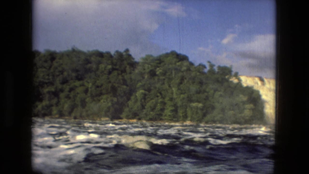 1979 Manaus, Brazil 8mm frame showing churning river water, a wooded bank, bright sky, and dark window-frame borders.