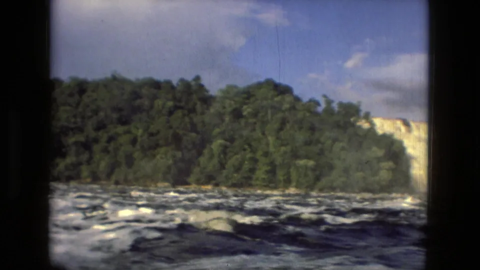 1979 Manaus, Brazil 8mm frame showing churning river water, a wooded bank, bright sky, and dark window-frame borders.